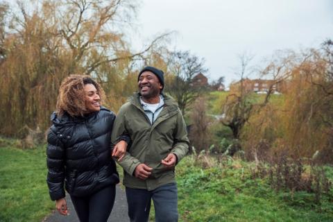 A man and a woman walk, arms linked, along a path through green space.